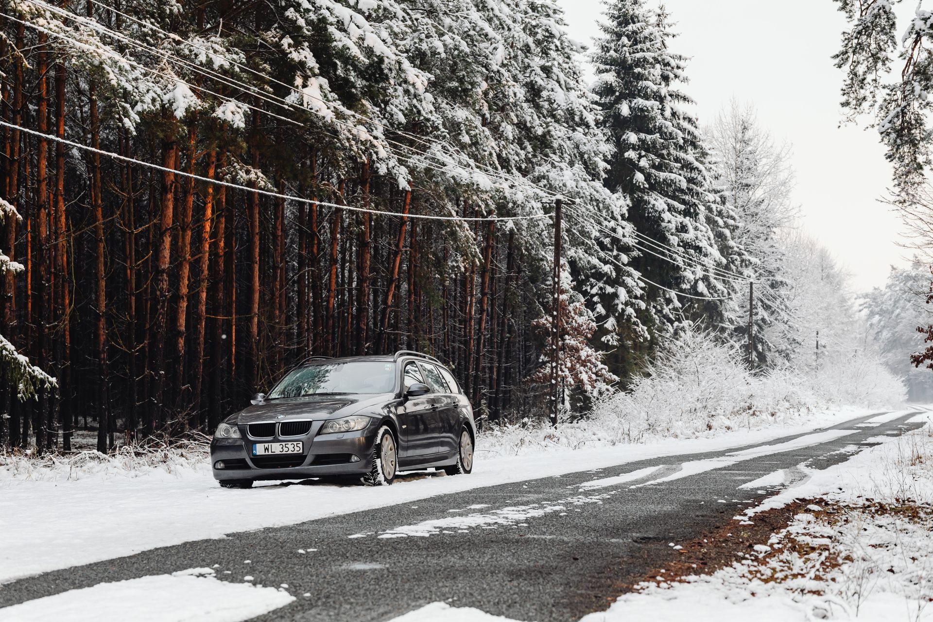 Fahrzeug auf verschneiter Straße vor einem winterlichen Wald.
