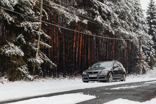 Free A car parked on a snowy roadside with snow-covered trees lining the serene winter road. Stock Photo