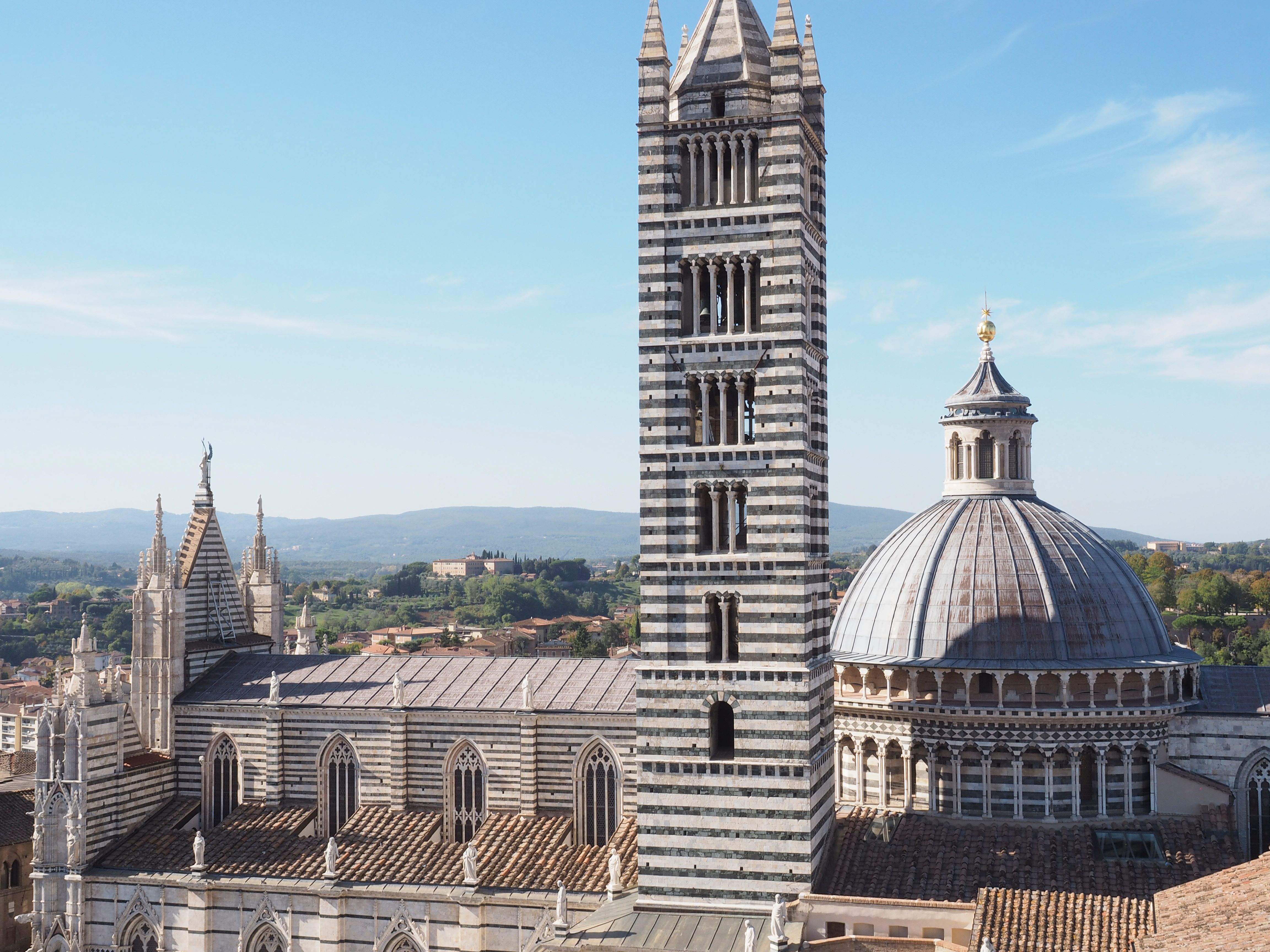 Siena Cathedral with its iconic striped bell tower and dome on a sunny day.