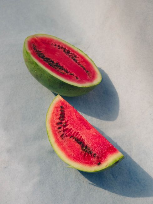 Two fresh watermelon slices on a light surface, showcasing vibrant red flesh and seeds.