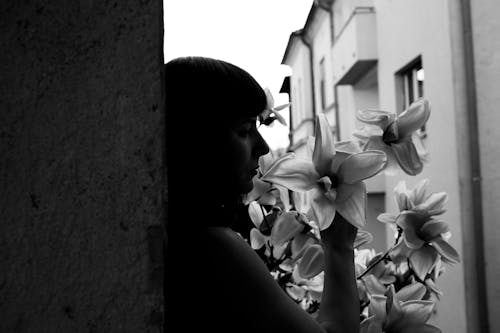 Free Upset woman smelling lily flower standing near concrete wall Stock Photo