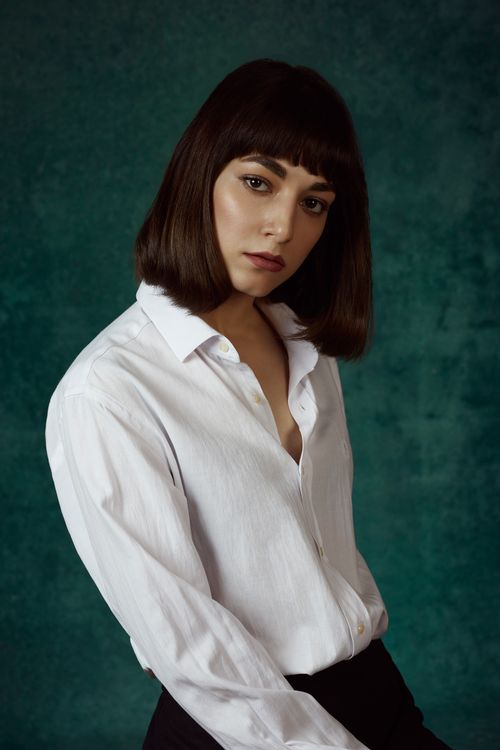 Free Sophisticated portrait of a woman in a white shirt against a dark green background, capturing elegance. Stock Photo