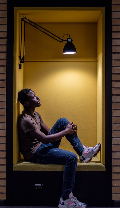 A Man Sitting in a Wall Recess Under a Lamp 