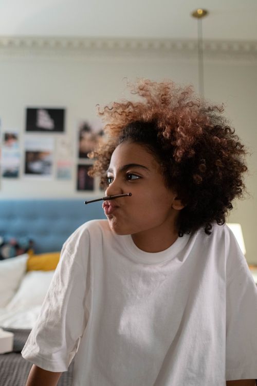 Free A joyful teenager with curly hair playfully holding a pen on her lips indoors. Stock Photo