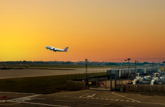 Airplane ascending during sunset at Heathrow Airport, capturing the vibrant sky.