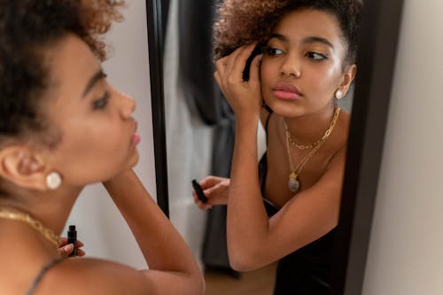A Woman Facing a Mirror Putting Mascara