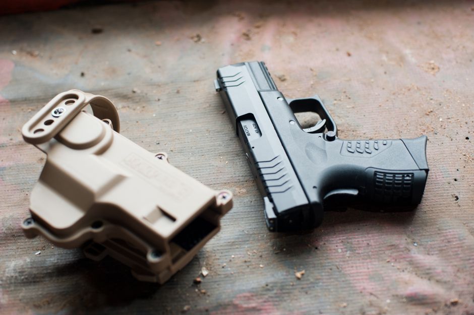 Close-up of a black handgun and beige holster on a textured surface, showcasing firearm details.