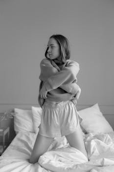 A woman relaxing on a bed, casually dressed in a sweater and shorts in a minimalist bedroom.