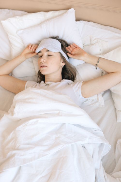 Free A woman sleeping soundly in bed with a white eye mask and cozy linens for a restful night. Stock Photo