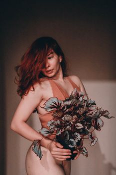 Side view of fit red haired female showing curves standing with potted plant and looking down