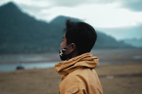 Man in Yellow Coat and Black Face Mask Looking at the Mountains
