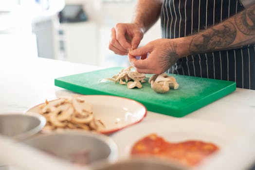 A tattooed chef skillfully prepares mushrooms on a green chopping board in a modern kitchen.