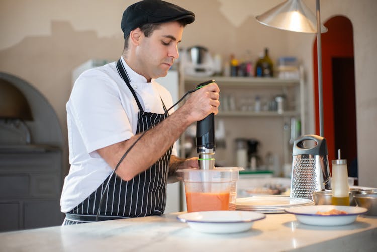 Chef Holding And Using Hand Blender Standing On Kitchen Counter