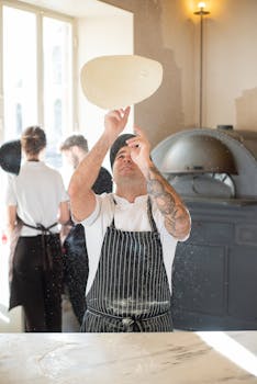 A chef in a traditional Portuguese bakery tosses pizza dough with skill, illuminated by natural daylight.