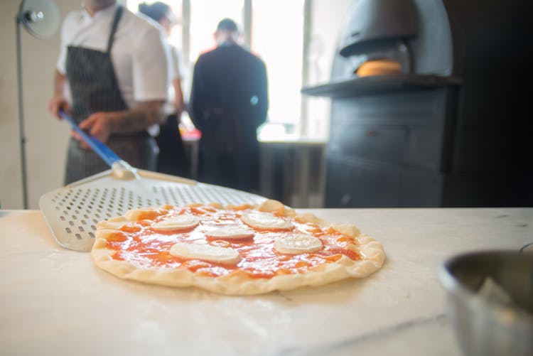 Baker Placing Pizza On A Table Using Pizza Peel