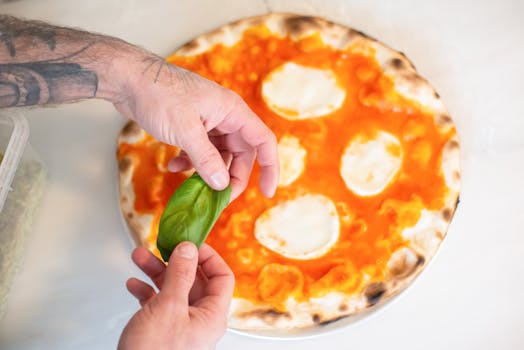 Close-up of hands adding basil to freshly baked pizza with mozzarella and tomato sauce.
