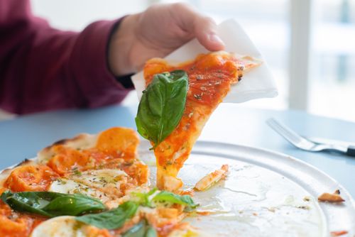 Free Close-up of a hand holding a slice of delicious Margherita pizza with basil topping on a sunny day. Stock Photo