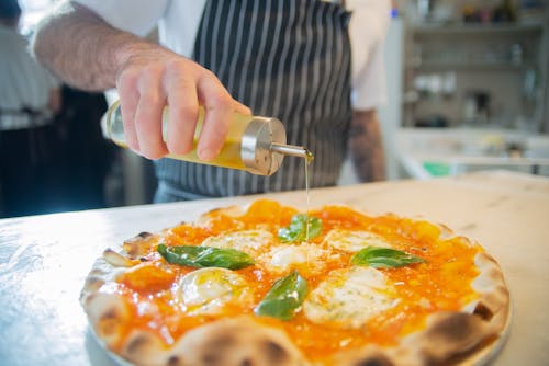 A Person Pouring Olive Oil on Pizza