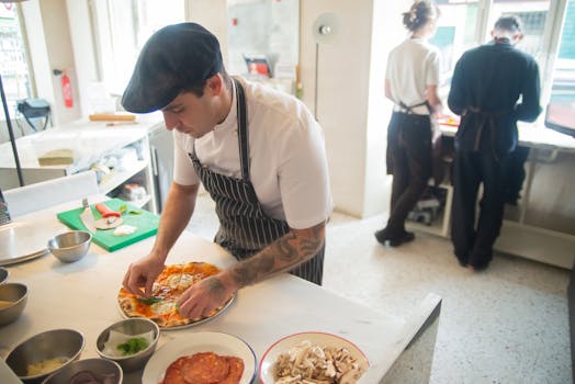 Chef preparing pizza in a professional kitchen setting, adding fresh ingredients to the dish.