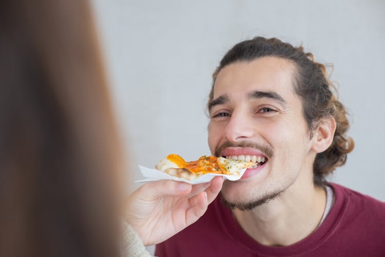 A Man Biting A Pizza On A Persons Hand