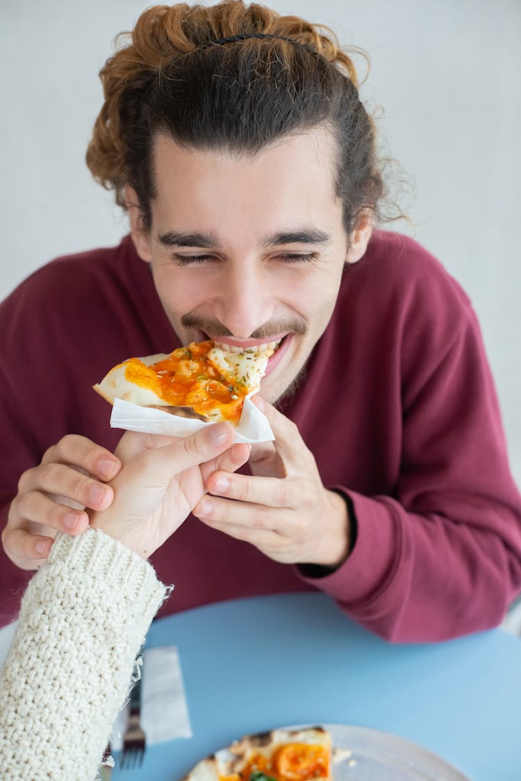 A Man Biting A Pizza On A Person's Hand