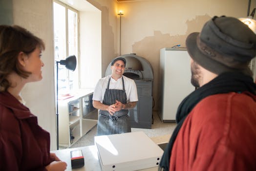 A cheerful chef engages with a couple in a cozy pizzeria, creating a welcoming atmosphere.