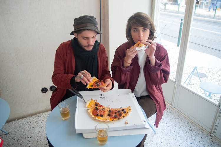 Couple Sitting Together On A Table Eating Pizza