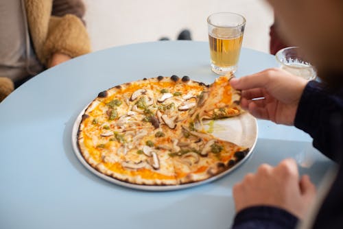 A Person in Black Long Sleeve Shirt Holding a Slice of Pizza on a Round Tray