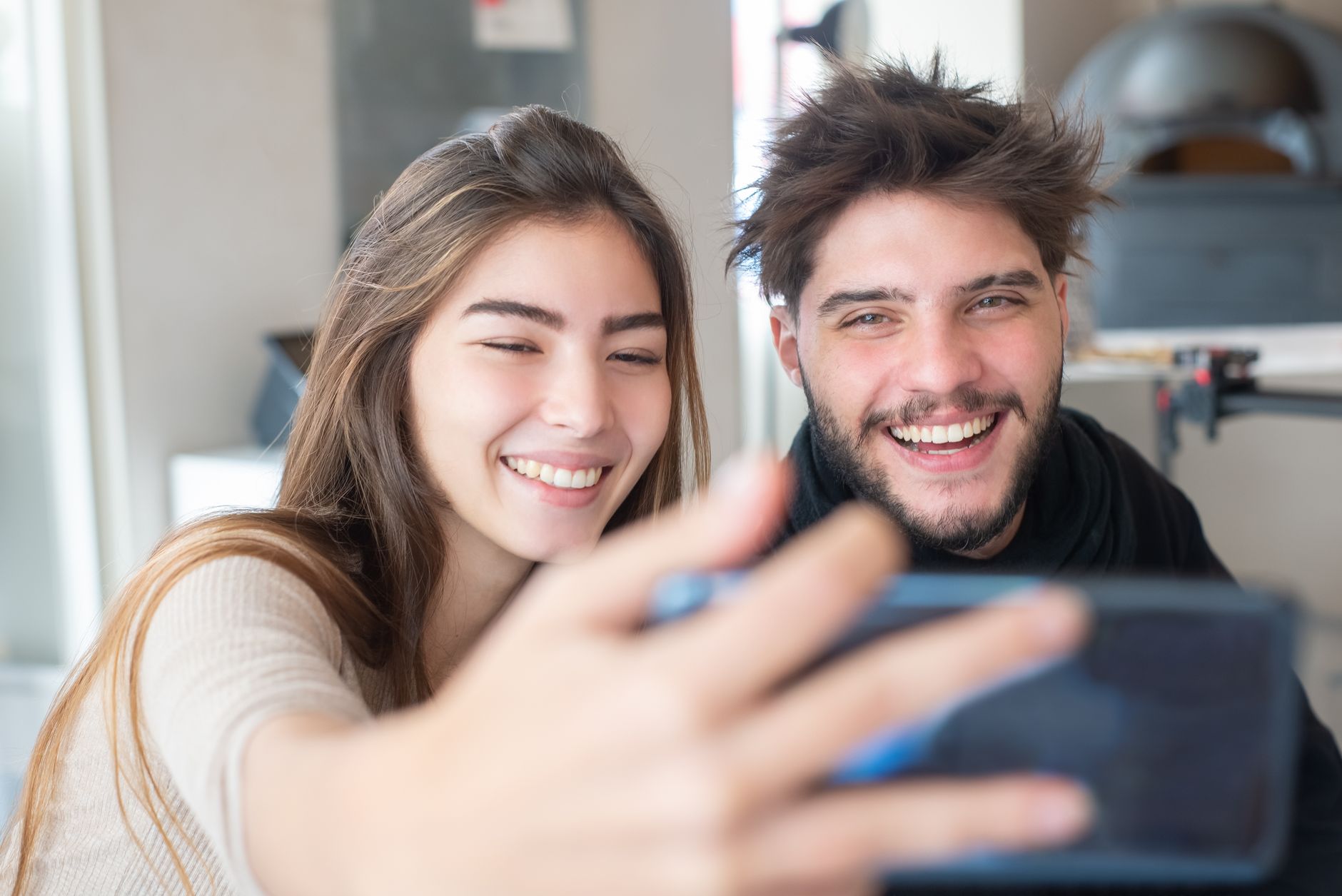 Happy young couple taking a selfie indoors, capturing joyful moments together with a smartphone.