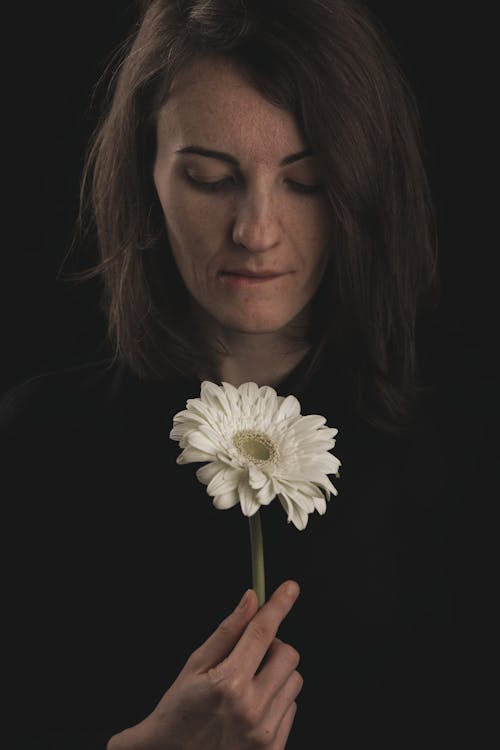 A Woman in Black Shirt Biting her Lip Holding a White Gerbera Daisy