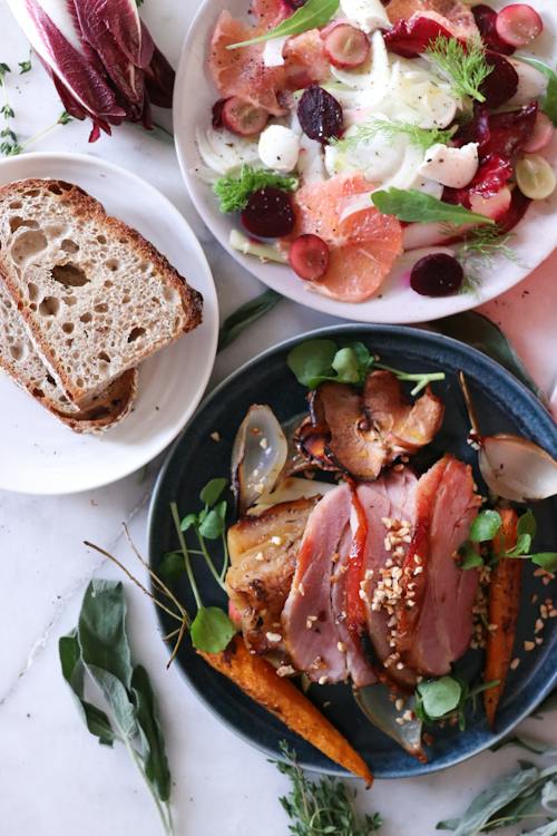 Top view of bowl with slices of meat with grilled vegetables and fruit placed on table near salad and bread