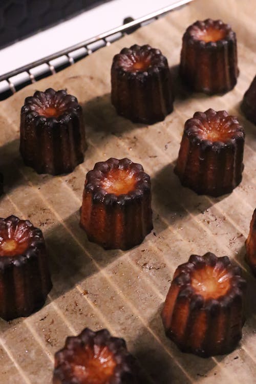 From above of appetizing sweet baked caneles with tasty caramel crust placed on metal baking pan with parchment in kitchen