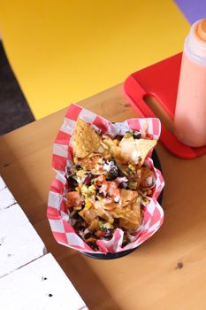 From above of Mexican fast food with tortilla chips and vegetables topped with cheese sauce served on plate with paper on table in cafe