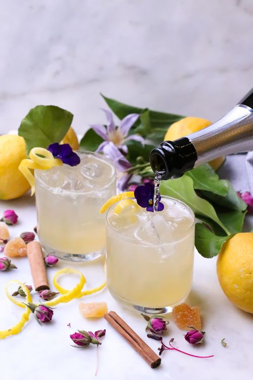 Free Transparent glasses with sparkling champagne decorated with flowers and zest placed on table with cinnamon near sour lemons with green leaves Stock Photo