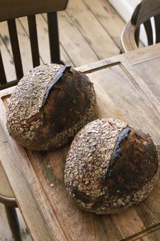 From above of fresh baked loaves of bread with crispy crust placed on wooden table in light room with chairs