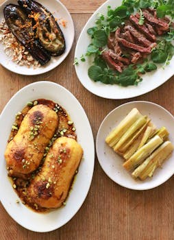Top view of grilled pumpkin and eggplant served on plates near platter with slices of meat decorated with herbs in kitchen