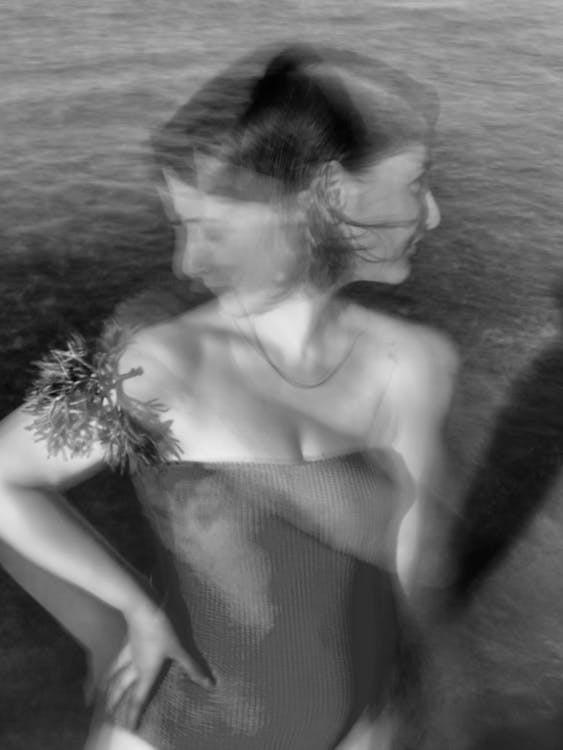 Black and white double exposure of female with hand on waist in swimwear standing on shore near rippling sea in nature