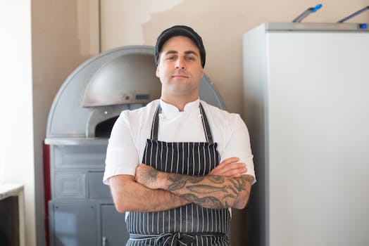 Portrait of a tattooed chef with crossed arms in a modern kitchen setting. Perfect for culinary and lifestyle concepts.