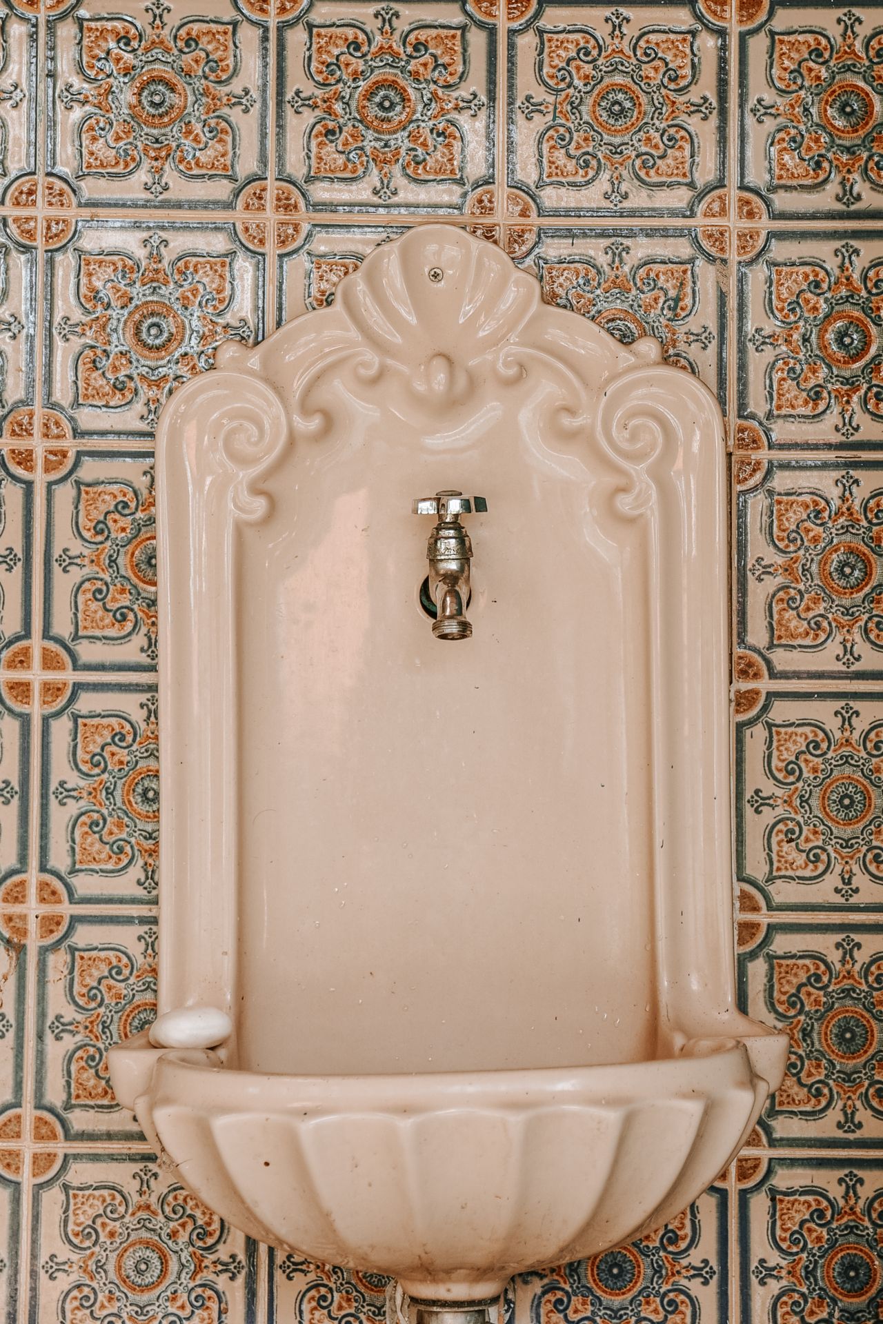 Vintage ceramic wall sink against hand-painted patterned tiles in rust, teal and cream, a classic Talavera tile look