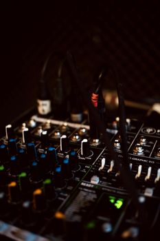 A detailed close-up of a dark, professional audio mixing console with various knobs and controls.