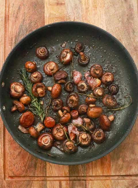 A stainless steel skillet of dark green sauteed spinach flecked with sliced garlic, tongs resting on the side of the pan.