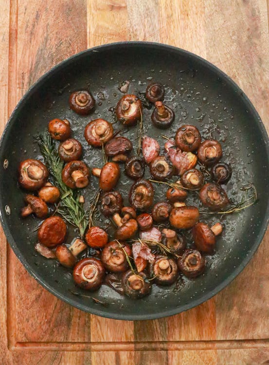Free Top view of many little tasty mushrooms in frying pan with green rosemary and garlic placed on wooden table in kitchen Stock Photo