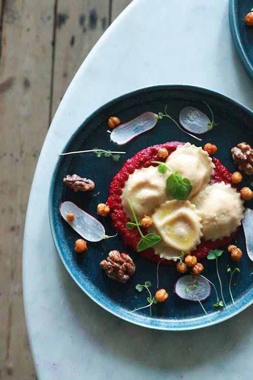 Free Top view of delicious ravioli with creamy beetroot sauce served on plate with radish slices and nuts in restaurant Stock Photo