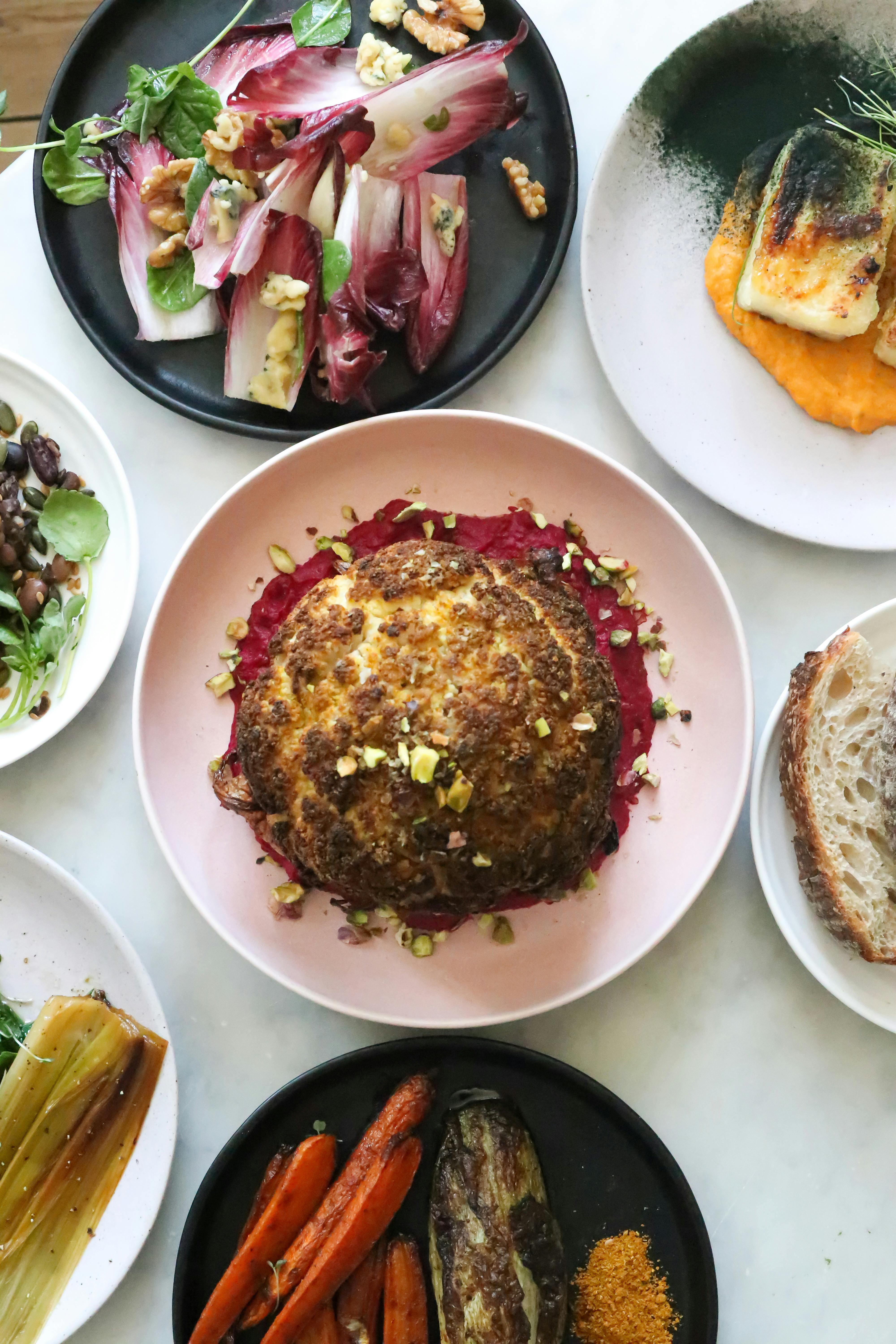Top view of whole roasted cauliflower dish with grilled carrots and eggplants served on table with various vegetable salads in restaurant