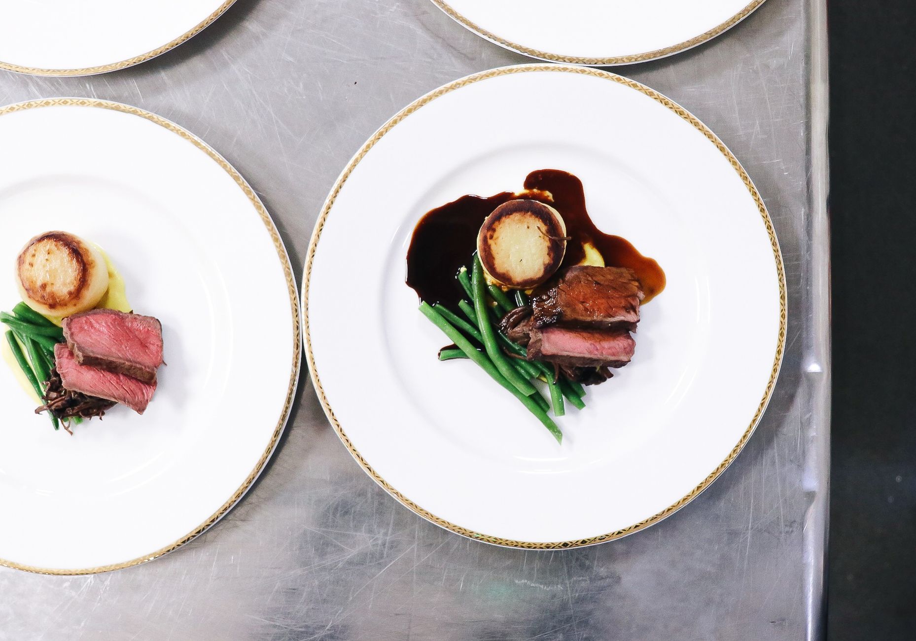 Top view of cut roasted meat near pan fried polenta and green beans with sauce on white plates on table in light restaurant