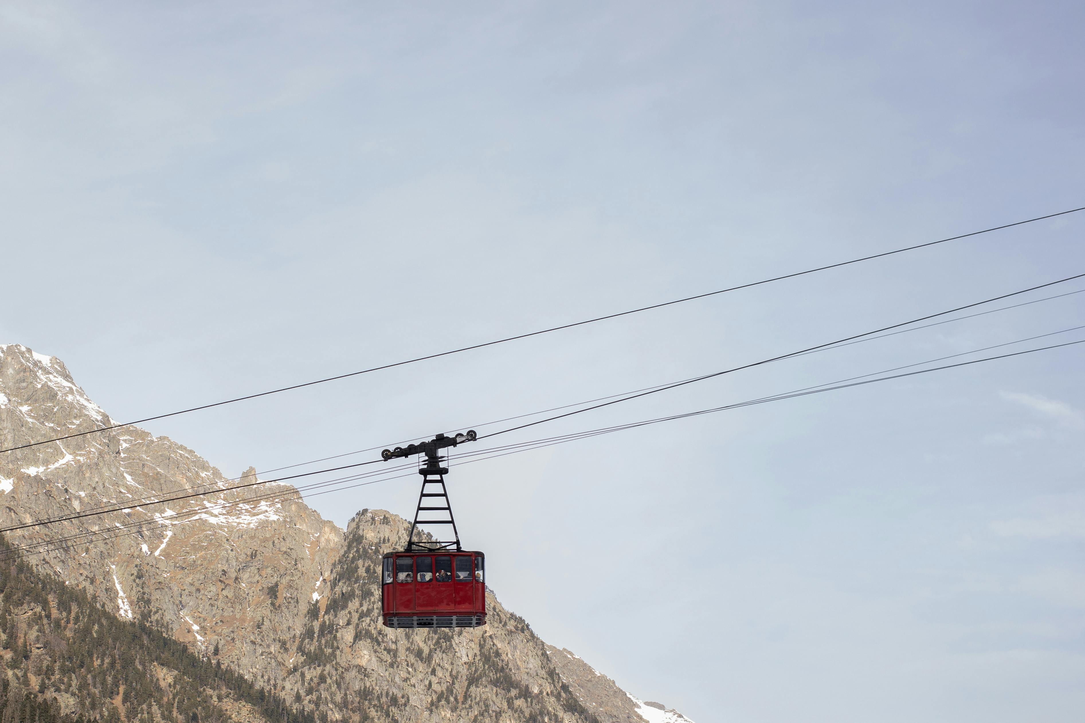 Prescription Goggle Inserts - A red cable car traversing a mountainous landscape under a clear sky.