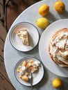 Tart with meringue on plates near lemons on table