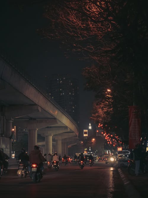 People Riding Motorbikes on the Road Under the Bridge