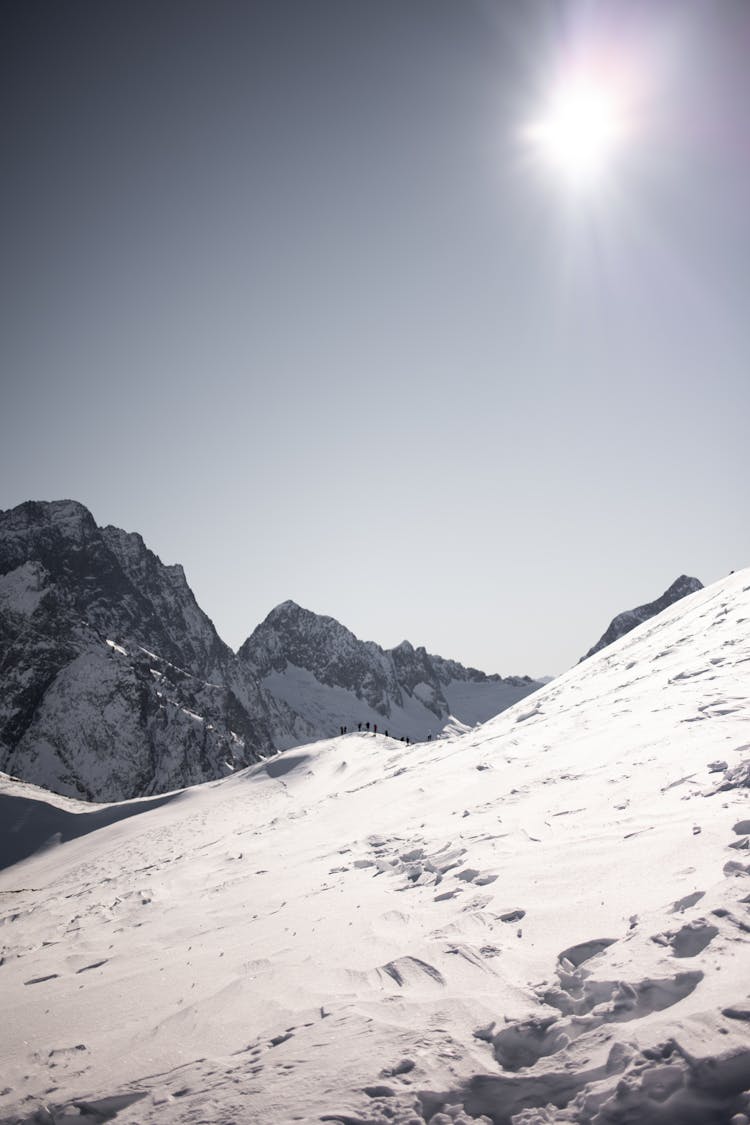 People Walking On A Snow Covered Mountain Under A Bright Sun