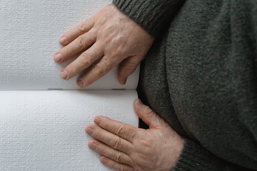 Close-Up Shot of Hands on a Braille Book 